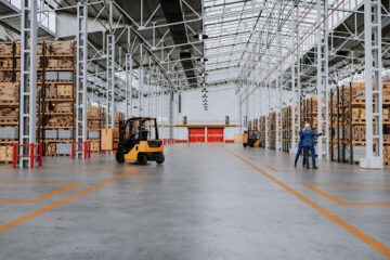 Galpão logístico com empilhadeiras, prateleiras altas e trabalhadores em operação.